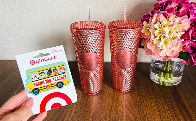 A Person Holding a Target Teacher Appreciation Gift Card in Front of Two Rose Gold Starbucks Tumblers on a Table