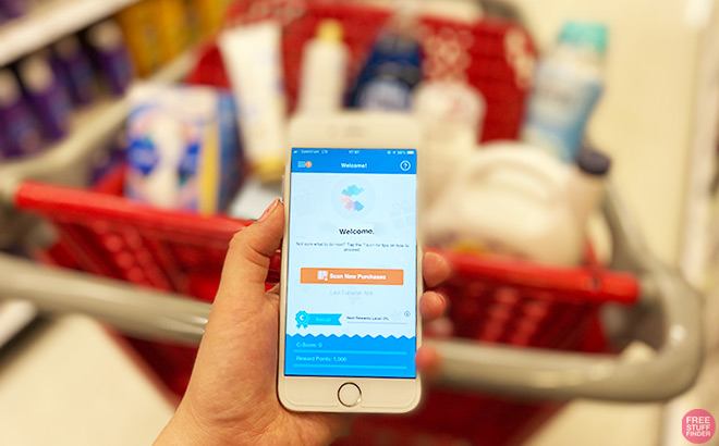 Hand Holding Phone with National Consumer Panel in Front of a Full Shopping Cart